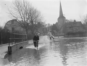 Bicycle Prints: Flooding in Eynsford, Kent. Cyclist rides through the water. 1937