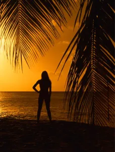 Paradise Prints: Girl on beach at sunset, seen through palm leaves