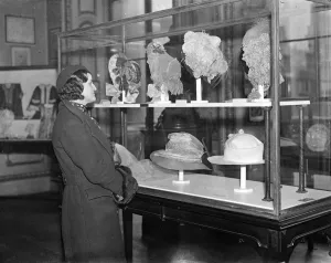 Girl in modern beret examines headgear of bygone days. 5 February 1935