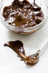 Sweet Prints: Glass bowl of melting chocolate with spoon smearing chocolate on white surface credit