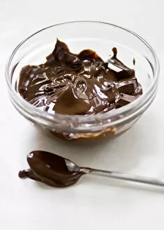 Ingredients Collection: Glass bowl of melting chocolate with spoon on white surface credit: Marie-Louise