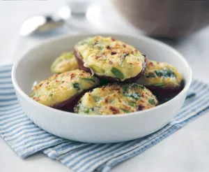 Halved baking potatoes baked with topping of cheese and spring onions credit: Marie-Louise