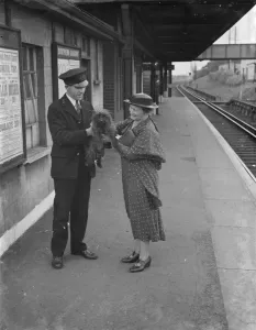 Crossing Prints: One happy dog is held aloft by a train station attendant with Mrs Boune Williams