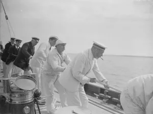The King takes the wheel of his yacht Britannia. The King assists in hauling the spinnaker