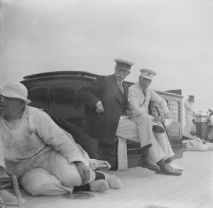 The King takes the wheel of his yacht Britannia. The Duke of Connaught and Sir