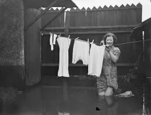 British Prints: Knee deep in flood water a housewife hangs out her washing at Maidenhead. 1 January