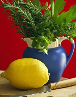 Savoury Collection: Lemon on chopping board with knife and bunch of mixed garden herbs in blue jug against