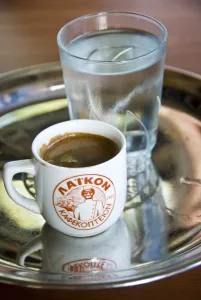 Glass Prints: Little cup of strong Greek coffee, with glass of water on tray on table of hillside