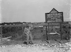 Fence Prints: A man by a protest sign in a derelict site at Kingsdown, Kent. 1935