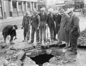 Ground Prints: Men stand around a mains water burst in Lee. 1936