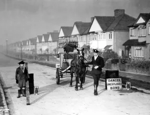 Fence Prints: Milk man with his horse and float stands in a street where an unexploded bomb has