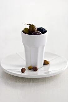 Olive Collection: Mixed Italian olives in tall white ceramic pot on white plate with stones on white