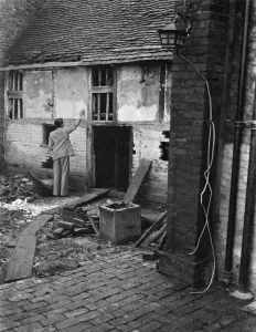 Ruin Prints: Mr Greenfield brushing the wall of an old dilapidated cottage to be used as a museum