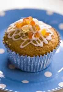 Muffin decorated with squiggly icing and candied peel on spotted blue plate credit