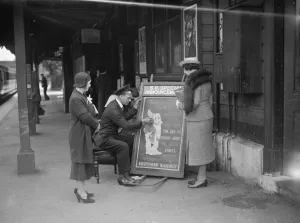 Fur Scarf Prints: People gather round to watch the railway porter sign writer Mr E A Burgar. 1938