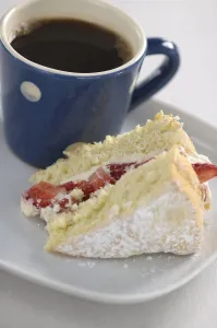 A piece of strawberry sponge cake on a white plate with a small blue and white spotted