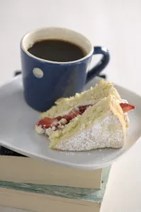 A piece of strawberry sponge cake on a white plate with a small blue and white spotted