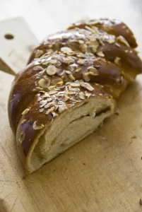 Piece of sweet, yeast bread with almonds and almond paste on wooden board credit