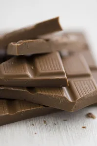Crumb Prints: Pile of broken pieces of mik chocolate bar on white surface. credit: Marie-Louise