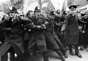 Policemen struggle to hold back the surging tide of demonstrators pressing on