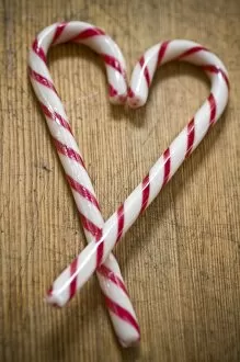 Shapes Collection: Two red and white striped candy canes on wooden surface crossed to make heart shape