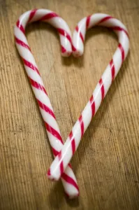 Two red and white striped candy canes on wooden surface crossed to make heart shape