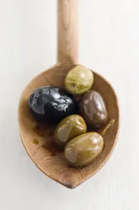 Whites Prints: Selecion of various good whole olives on rustic wooden spoon credit: Marie-Louise
