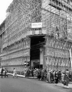 Construction Prints: Shoppers passing through a tunnel of tubular scaffolding an intricate network, like