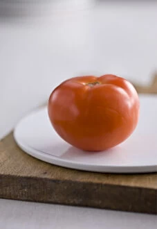 Ingredients Collection: Single red tomato on white platter on wooden board credit: Marie-Louise Avery /