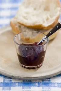 Glass Prints: Small glass bowl of seedless raspberry jam with crusty bread on old scrubbed board