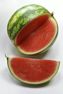 Ingredients Collection: Small watermelon on white surface with quarter cut out showing red flesh credit