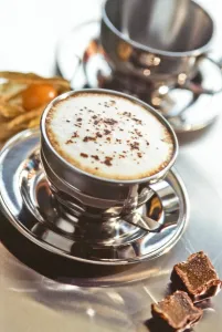 Coffee Prints: Stainless steel cup of cappucino on metal counter with chocolate fudge and pthysalis