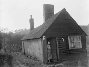 Wood Prints: A women stands in the doorway of a cottage that was once a mortuary
