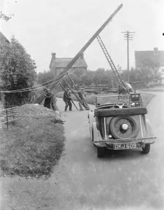 workers use ladders and poles erect an electric pylon next to a road in Trottiscliffe