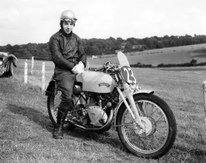 A young John Surtees sitting astride his Vincent motorbike at a race track